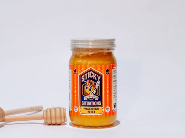 Image of 8 oz passionfruit honey jar with honey dipper to the left