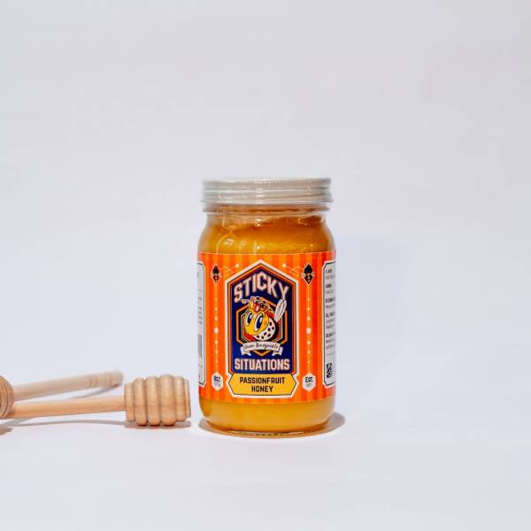 Image of 8 oz passionfruit honey jar with honey dipper to the left