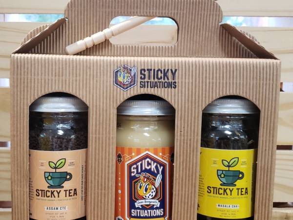 masala chai tea, assam ctc tea, and lemon honey in a box with the sticky situations logo and a honey dipper on top.