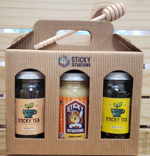 masala chai tea, assam ctc tea, and lemon honey in a box with the sticky situations logo and a honey dipper on top.