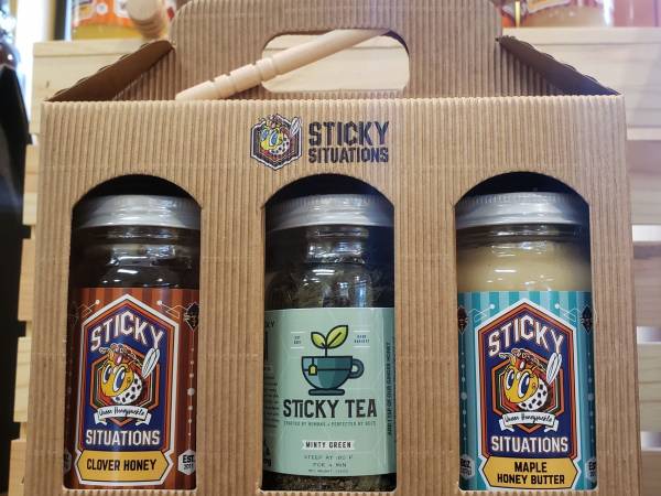 Clover honey, maple honey butter, and minty green tea in a box with the sticky situations logo and a honey dipper on top.