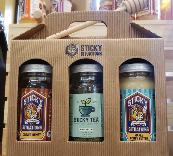 Clover honey, maple honey butter, and minty green tea in a box with the sticky situations logo and a honey dipper on top.