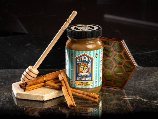 8 oz sticky situations cinnamon honey butter with cinnamon sticks and honey dipper to left