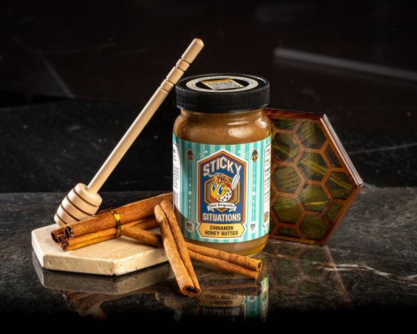 8 oz sticky situations cinnamon honey butter with cinnamon sticks and honey dipper to left